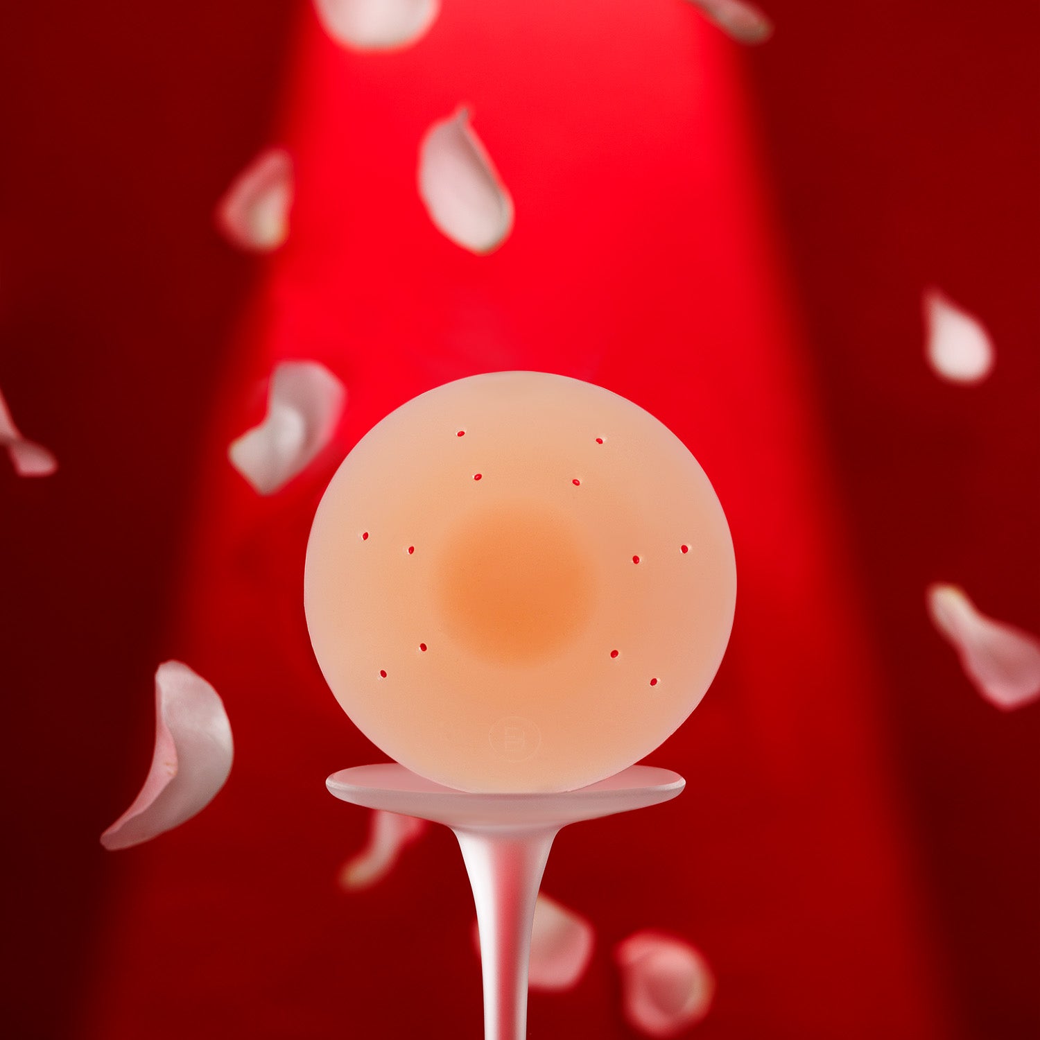 Essential silicone petal on white platform with falling petals, red background, and spotlight lighting.