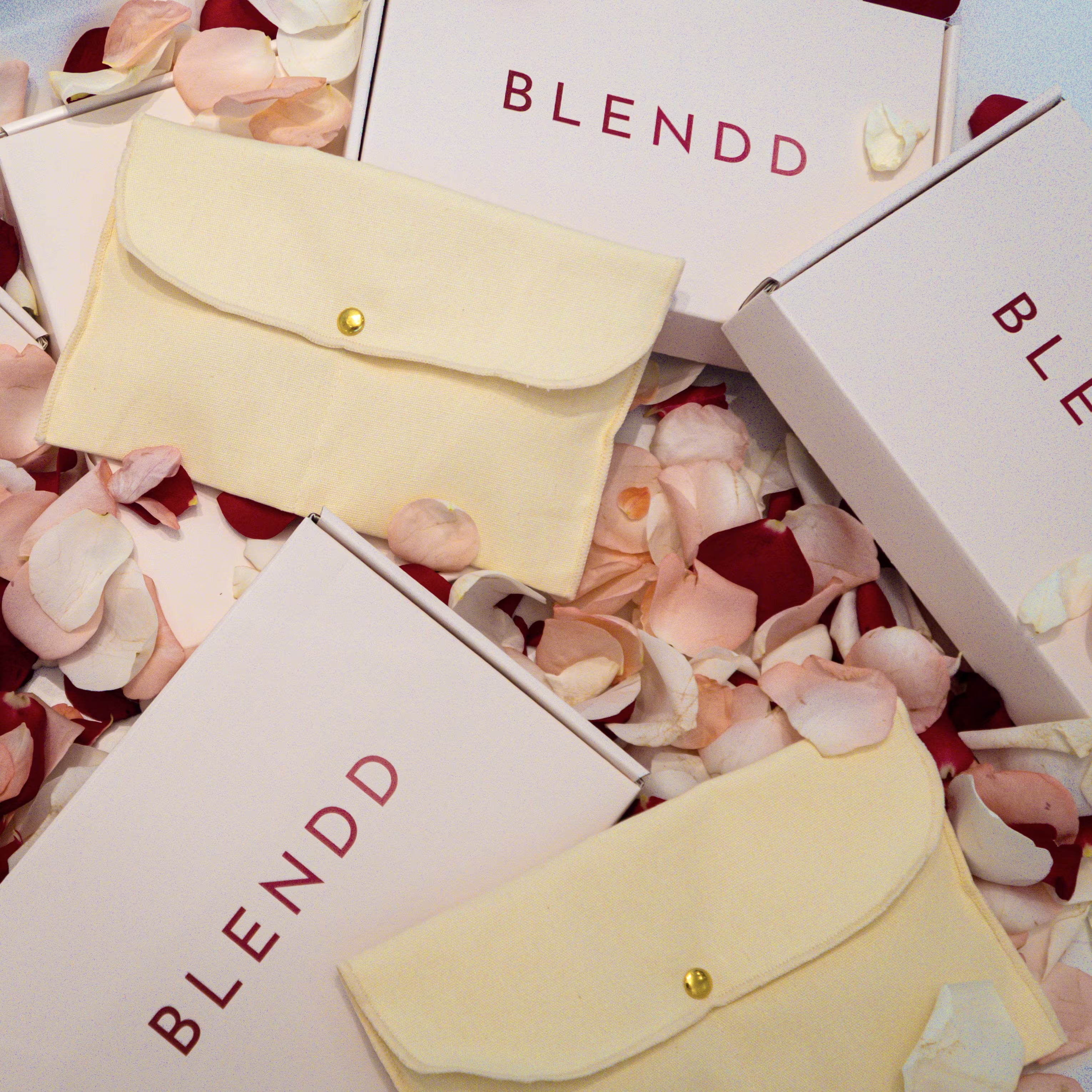 Yellow pouches with gold clasps on a bed of rose petals with 'BLENDD' branding.