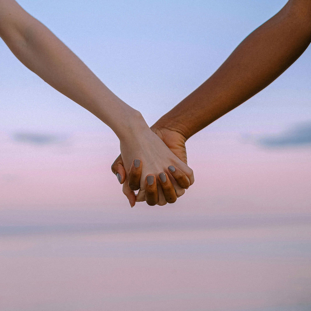 Two hands joining together against pink sunset sky symbolizing partnership