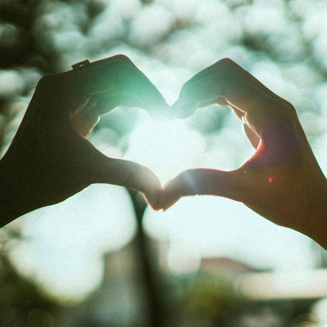 Hands forming heart shape silhouette against bright natural sunlight