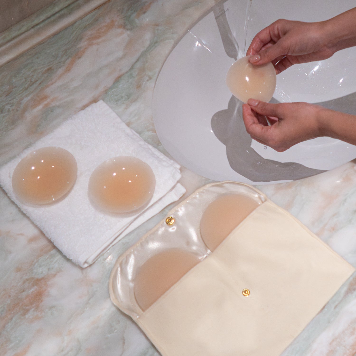 Hands washing silicone petals with two petals drying on white towel and two in storage pouch.